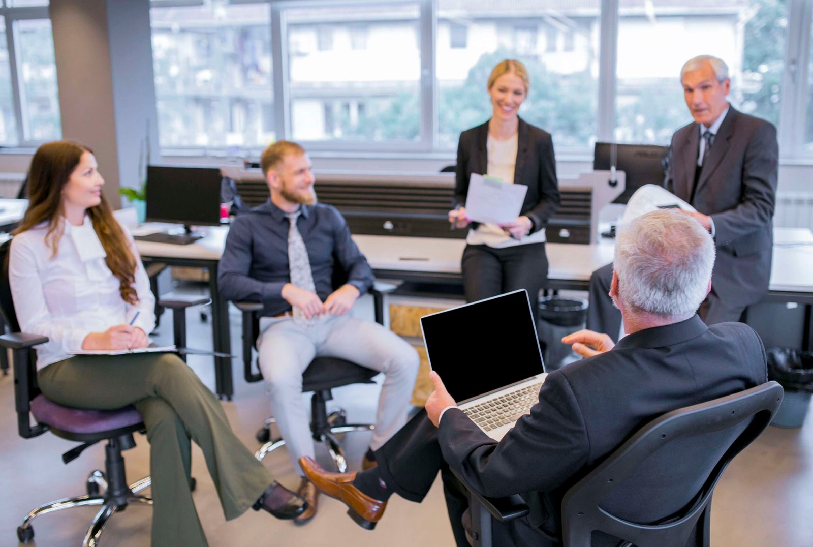 Senior businessman with laptop sitting in front of his team in an office